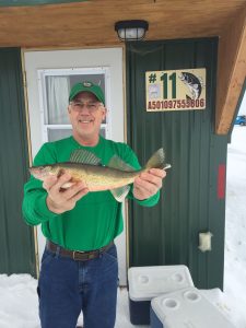 man holding fish in front of ice house