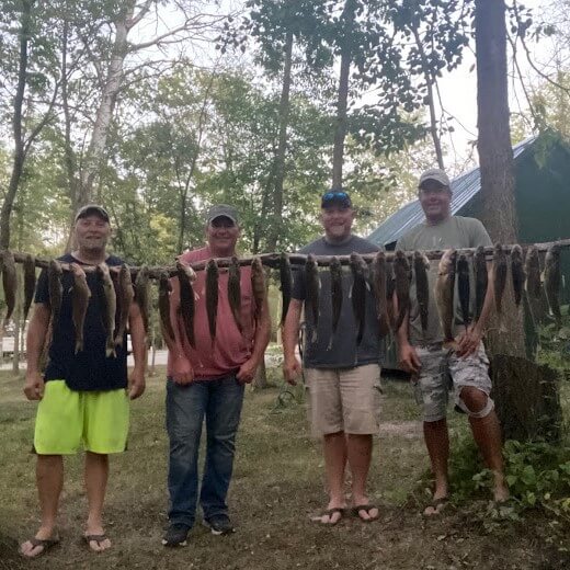 Four men stand behind a string of caught fish